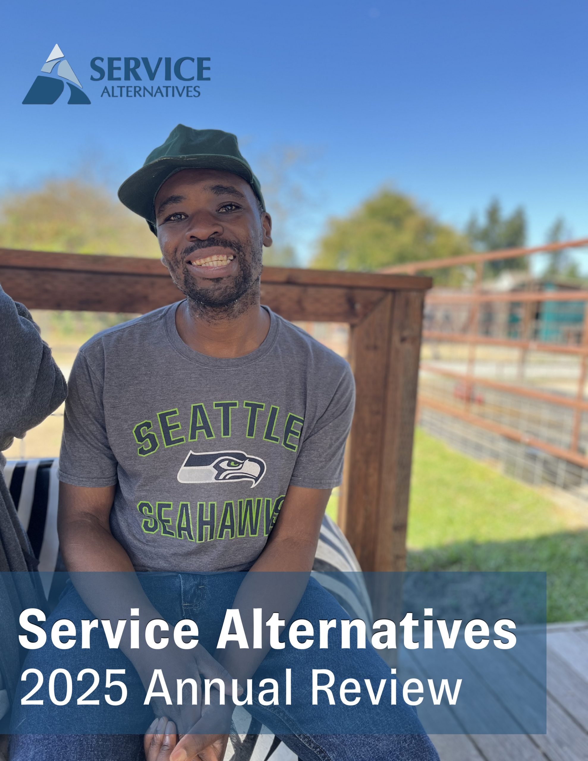 Smiling man in a Seattle Seahawks t-shirt sits on a wooden deck outdoors with a blue sky; logo reads 'Service Alternatives' in the top left.